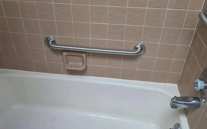 Stainless steel grab bar installed on tan tile above a bathtub